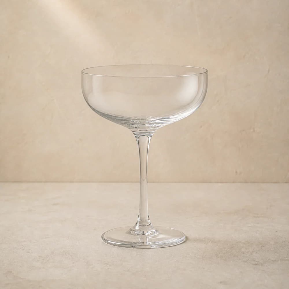 An empty clear coupe glass with a shallow rounded bowl and slender stem.