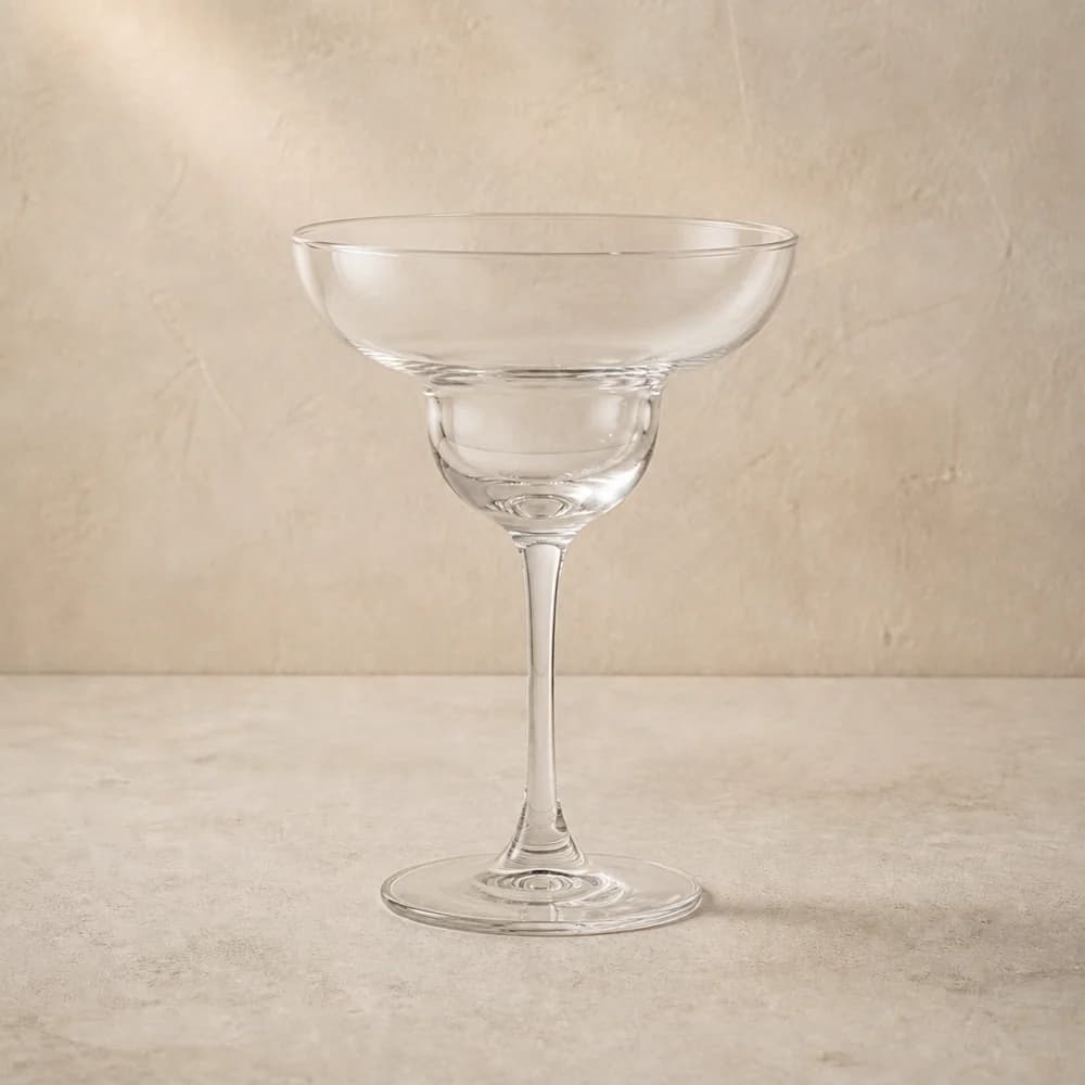 An empty clear margarita glass with a distinctive wide double bowl and slender stem.