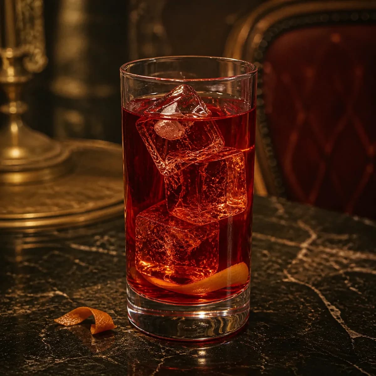 Brandy Milk Punch in a tall straight-sided highball glass styled in a Belle Époque salon bar with faded burgundy velvet, dark marble and aged brass.