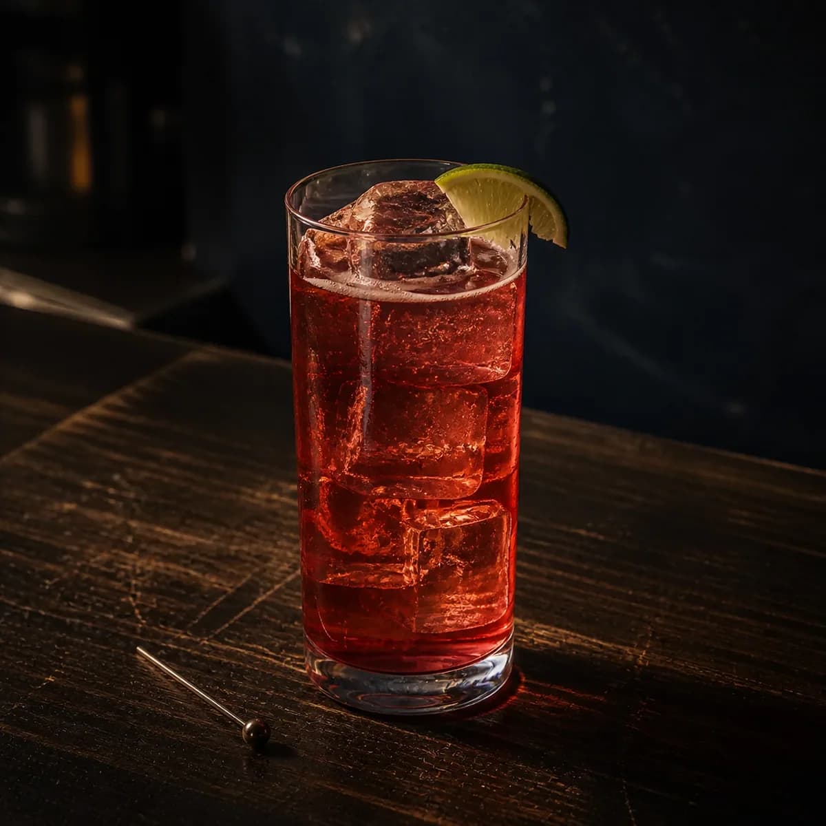 Cape Codder in a tall straight-sided highball glass styled in a late-night espresso bar with smoky navy limewash, scratched dark oak and restrained chrome highlights.