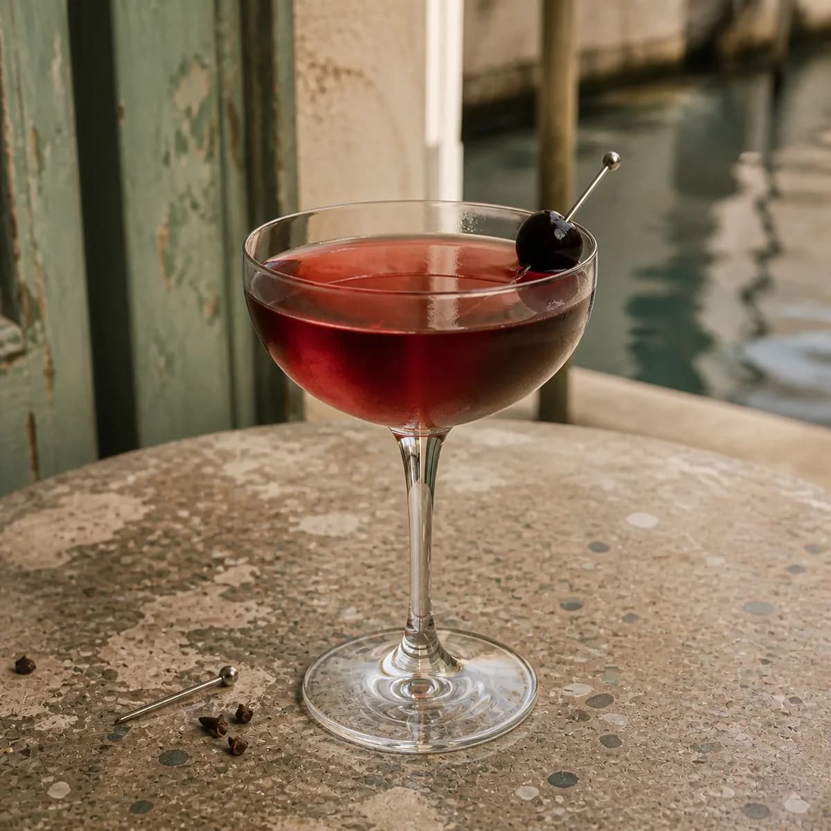 Diplomat in a clear shallow coupe styled in a quiet canal café bar with worn celadon paint, old terrazzo and watery reflections in the distance.