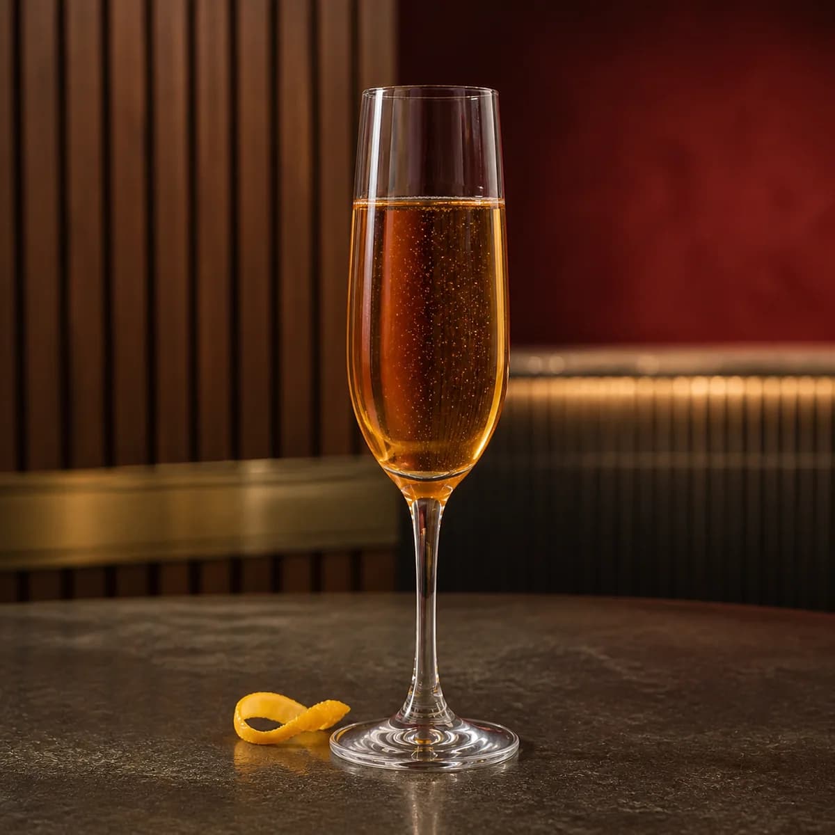 Kir Impérial in a slender champagne flute styled in a modern amaro bar with ribbed walnut, smoked red plaster and brushed pewter.