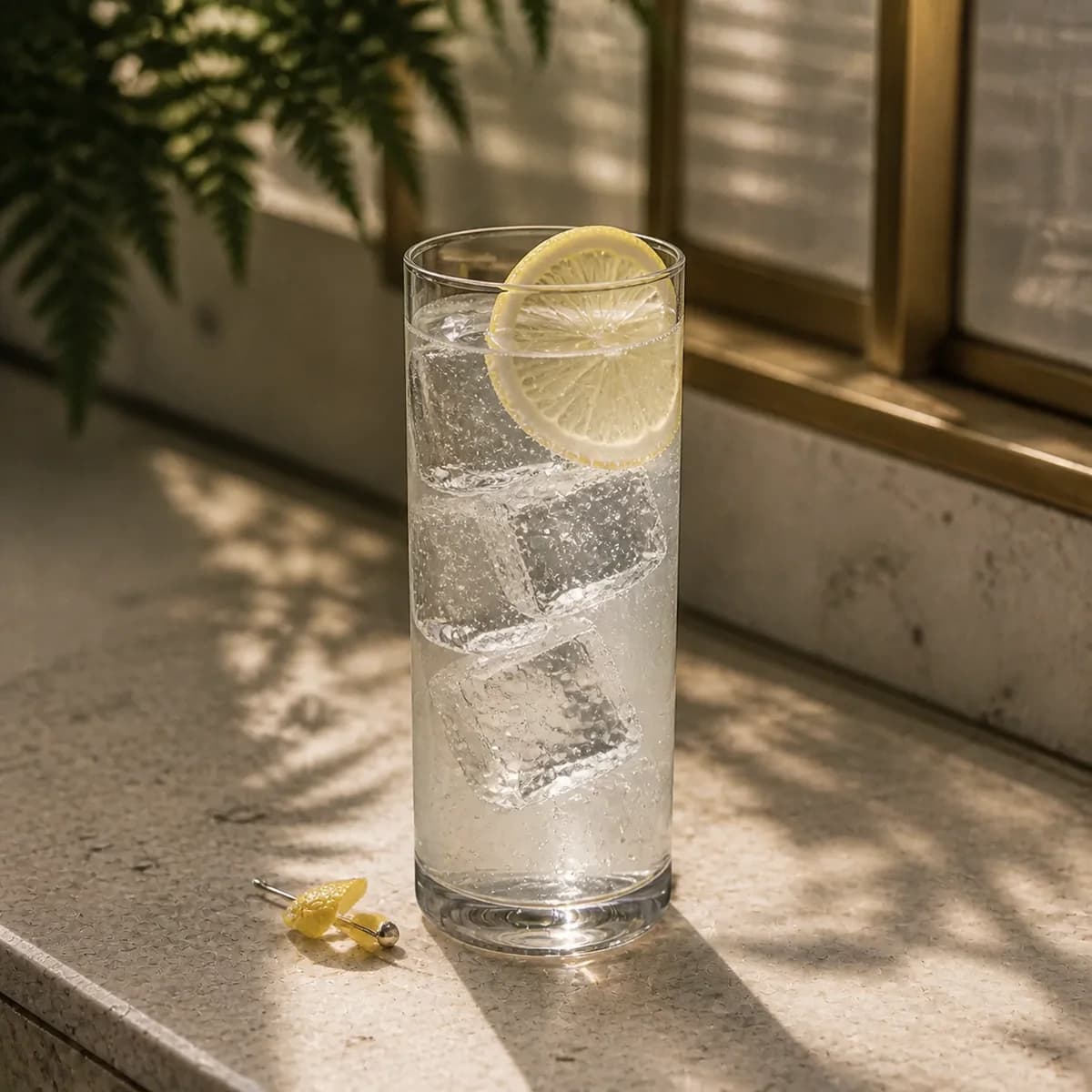 Remsen Cooler in a tall straight-sided highball glass styled in a glasshouse café bar with pale stone, fern shadows and lightly weathered brass.