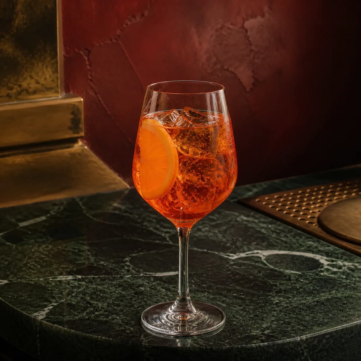Vermouth Cocktail in a heavy low rocks glass styled in a Milan aperitivo bar with oxblood hand-painted plaster, asymmetric aged brass and dark green marble.