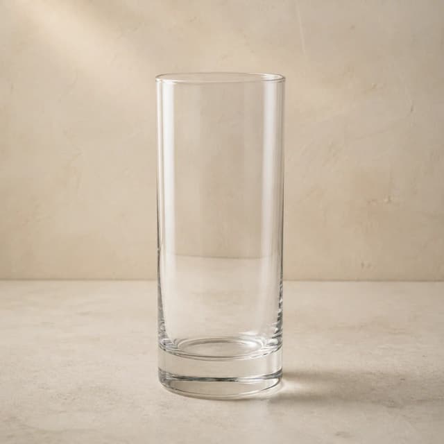 An empty clear highball glass with tall straight sides and a substantial base.
